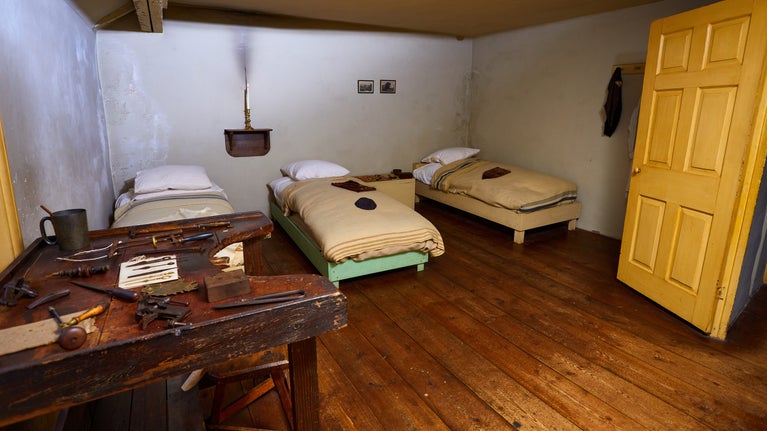 View of working people's bedrooms at Birmingham Back to Backs. Three beds are along one wall with a large workbench taking up another wall.